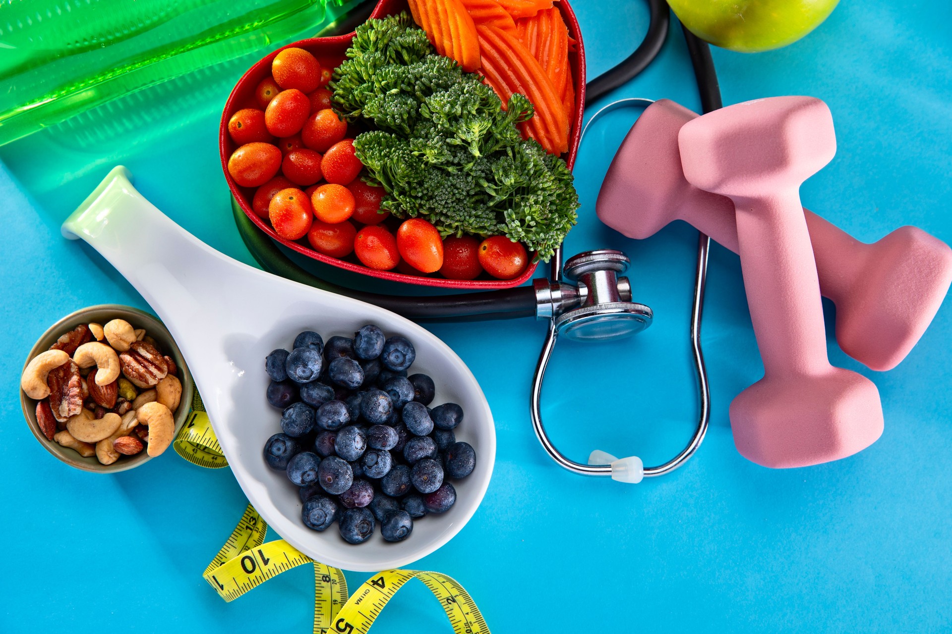 Vegetables in a heart bowl with dumbells and blueberries on a blue background